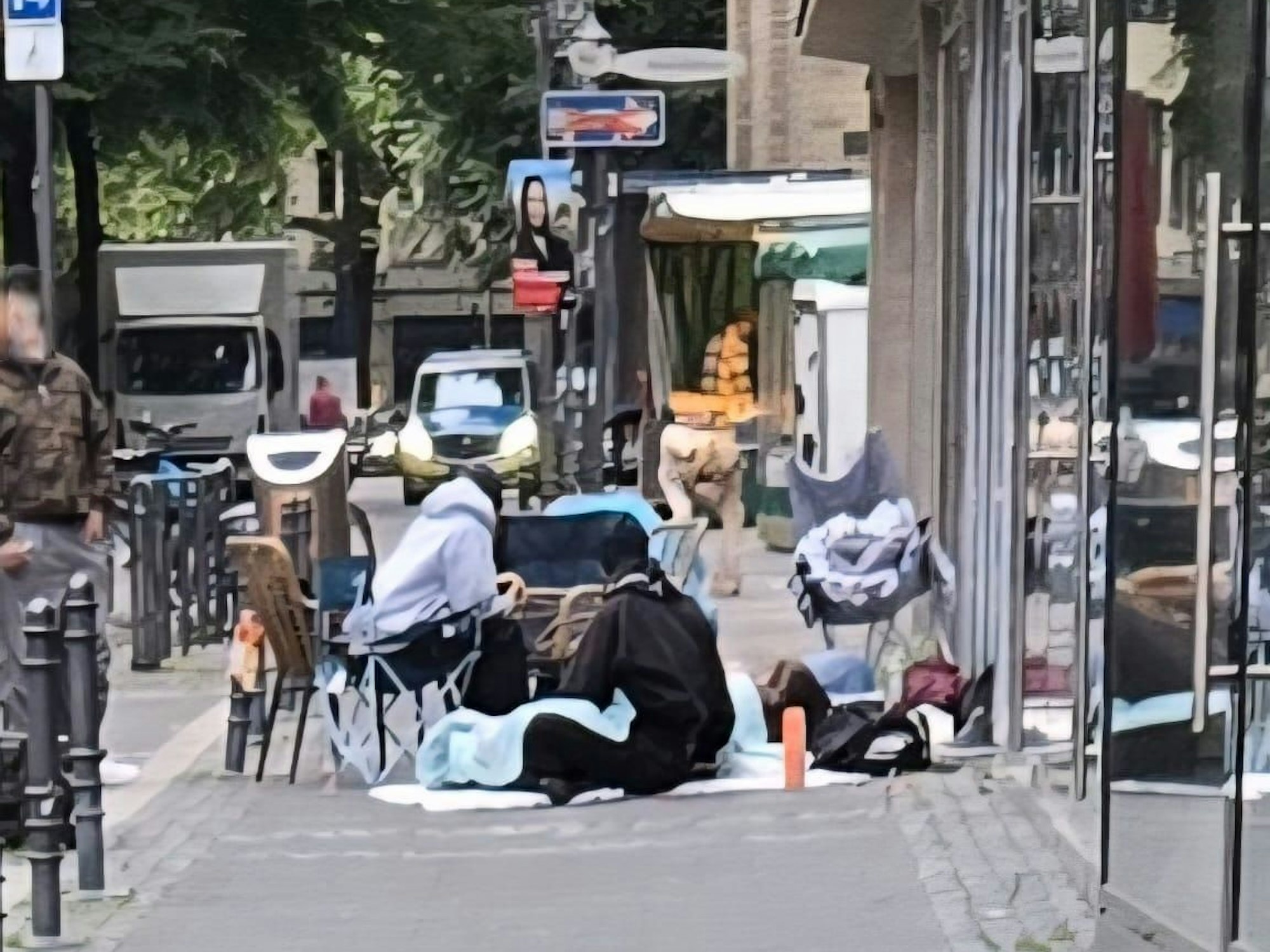 Mehrere Personen sitzen auf dem Gehweg vor einer Geschäftszeile.
