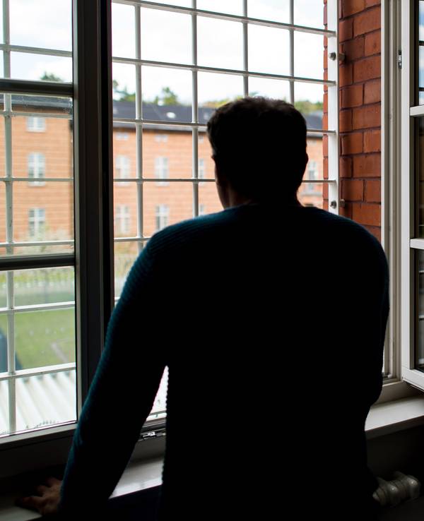 Ein Straftäter steht vor einem vergitterten Fenster in einer Klinik für Forensische Psychiatrie (Maßregelvollzug) auf dem Gelände eines Krankenhauses. (Symbolfoto)