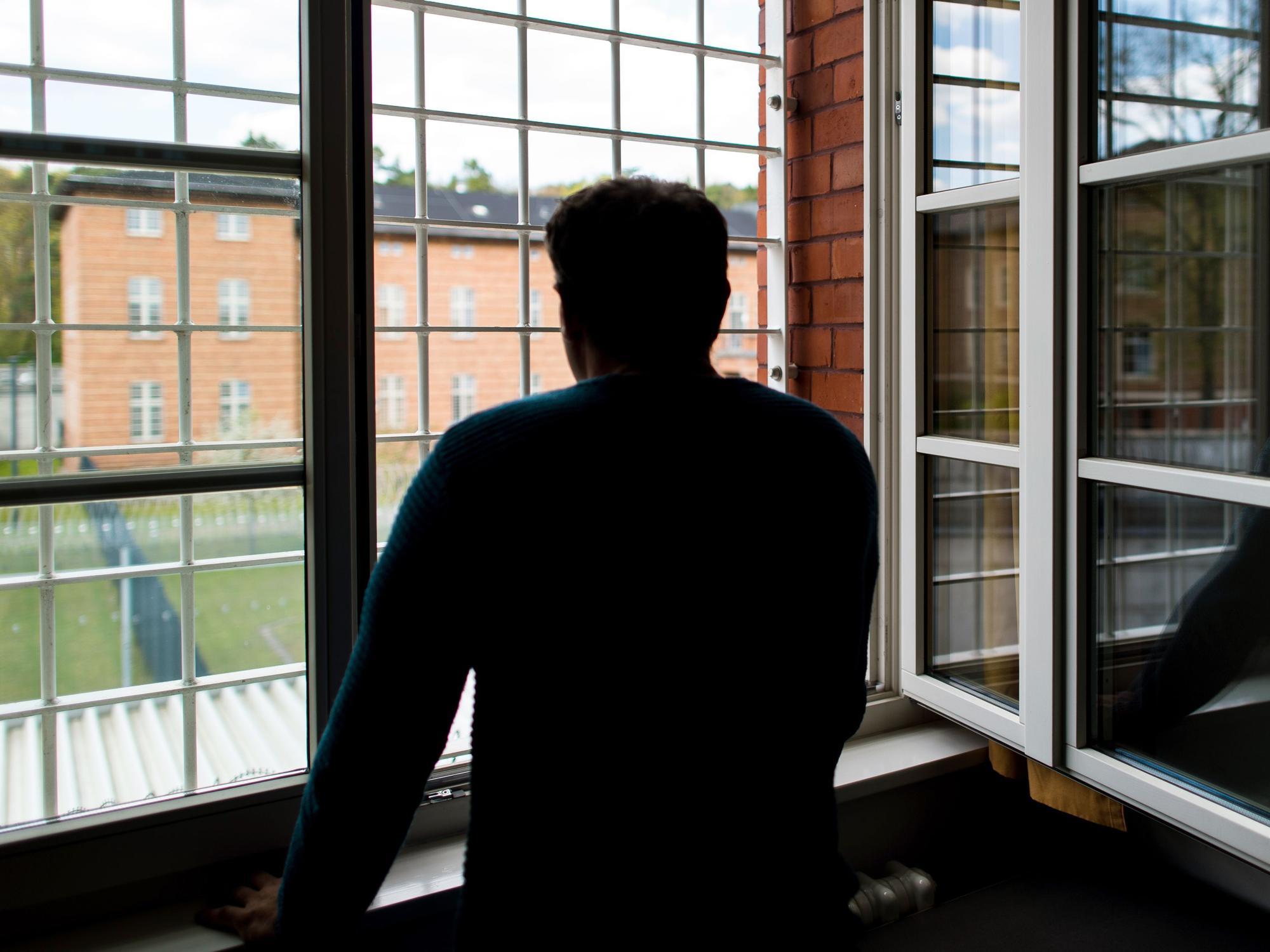 Ein Straftäter steht vor einem vergitterten Fenster in einer Klinik für Forensische Psychiatrie (Maßregelvollzug) auf dem Gelände eines Krankenhauses. (Symbolfoto)