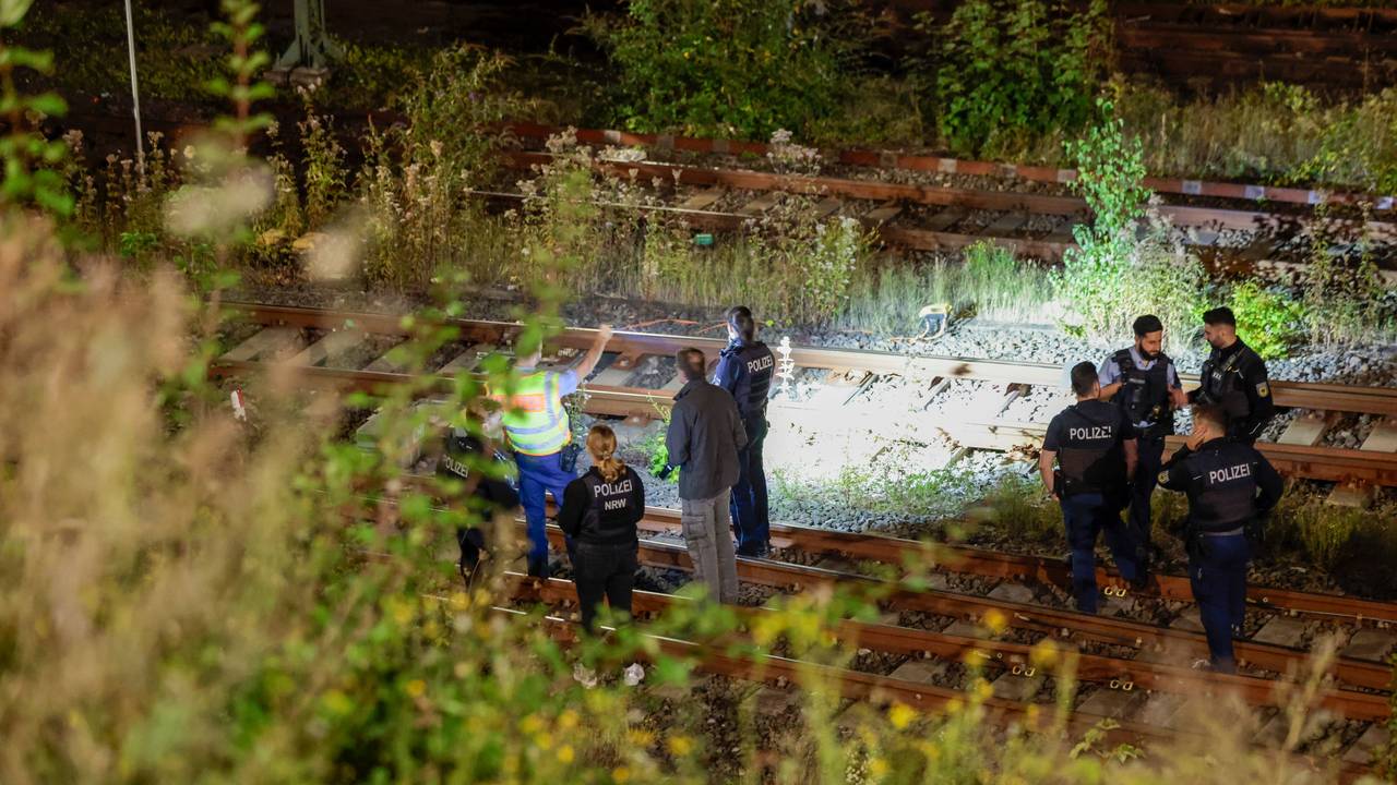 Einsatzkräfte der Polizei stehen nachts an Bahngleisen, einer leuchtet mit einer Taschenlampe auf eine Stell.