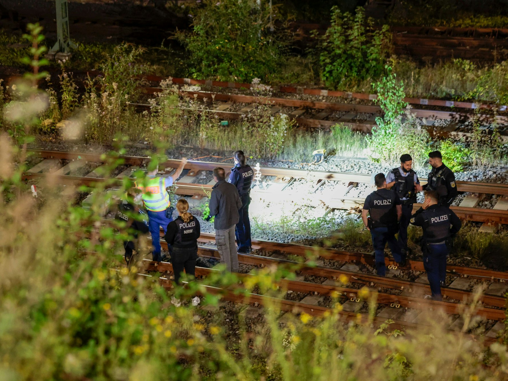 Einsatzkräfte der Polizei stehen nachts an Bahngleisen, einer leuchtet mit einer Taschenlampe auf eine Stell.