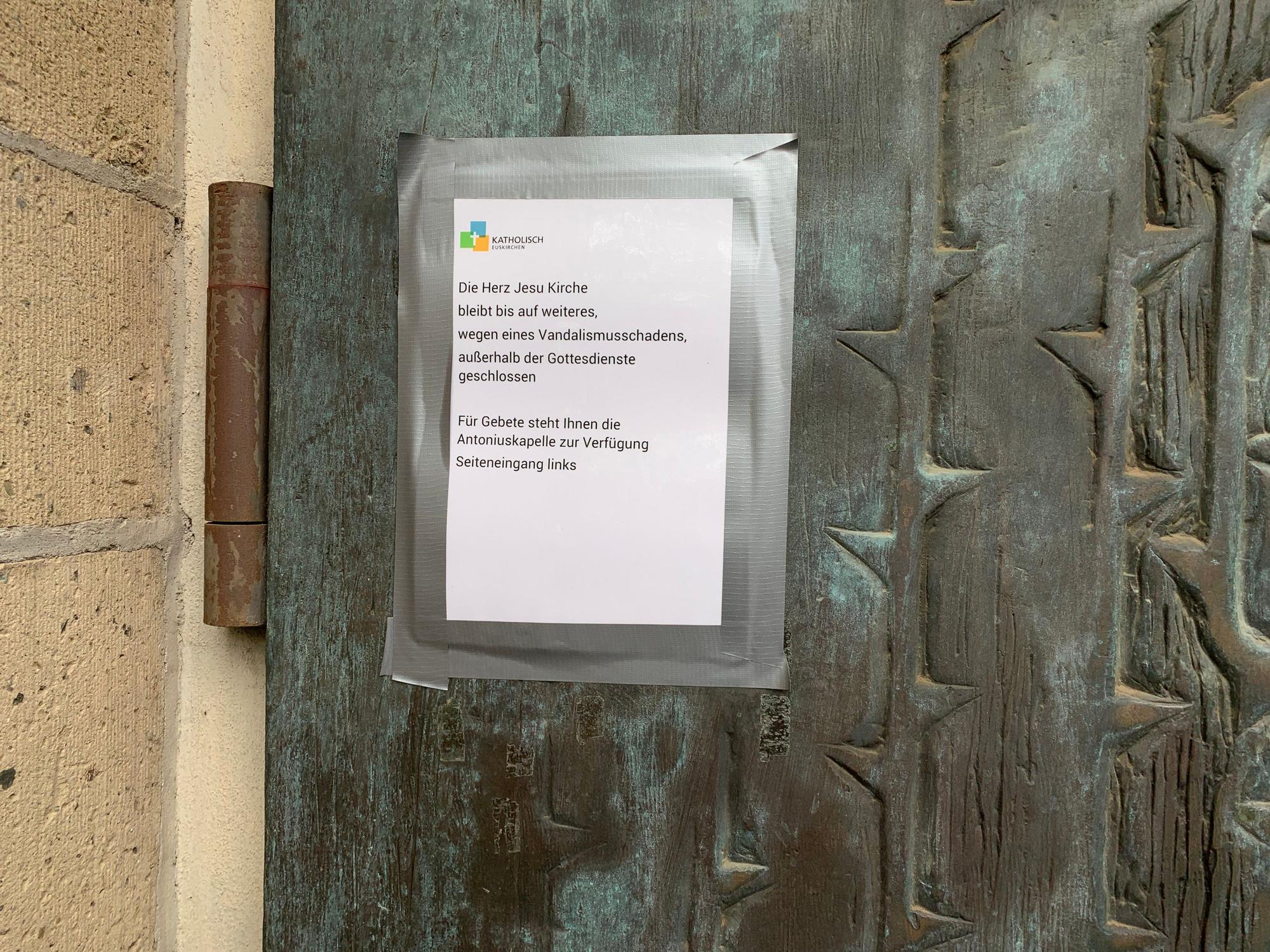 An einer Kirchentür hängt ein Zettel mit dem Hinweis: Wegen Vandalismusschäden bleibt die Herz-Jesu-Kirche in Euskirchen außerhalb der Gottesdienstzeiten geschlossen.