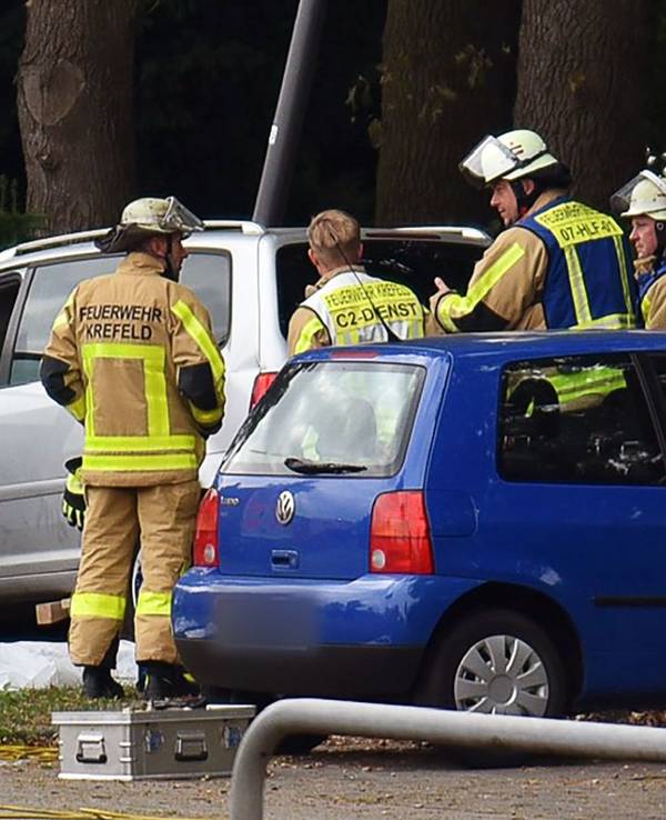 Kräfte der Feuerwehr stehen neben einem Auto, vor dem auf dem Boden etwas abgedeckt ist.