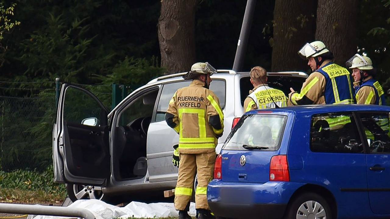 Kräfte der Feuerwehr stehen neben einem Auto, vor dem auf dem Boden etwas abgedeckt ist.