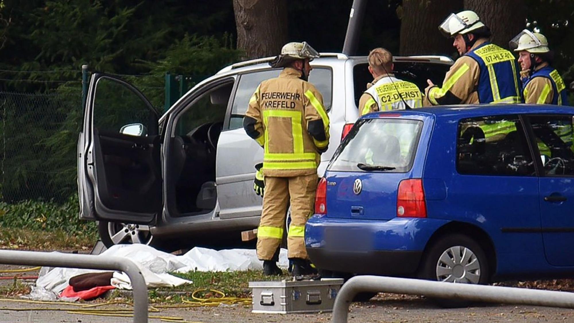 Kräfte der Feuerwehr stehen neben einem Auto, vor dem auf dem Boden etwas abgedeckt ist.