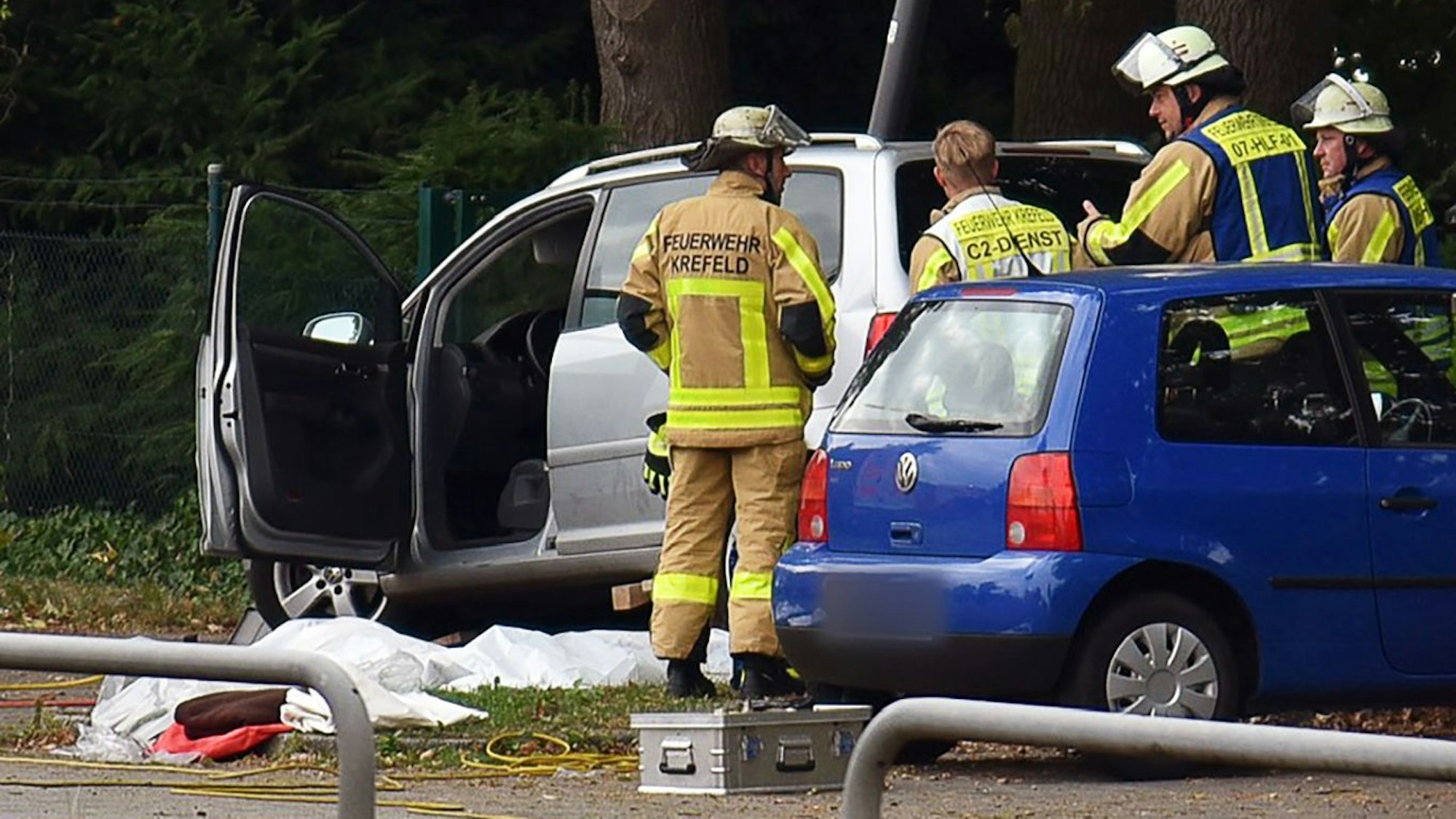 Kräfte der Feuerwehr stehen neben einem Auto, vor dem auf dem Boden etwas abgedeckt ist.