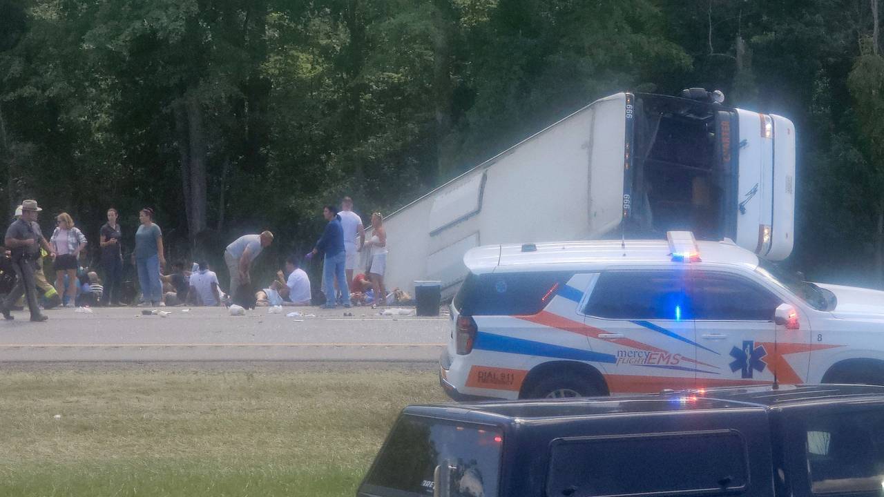 Ein Bus liegt mit der Front voraus in einem Graben, neben ihm stehen mehrere Menschen. Auch ein Polizeifahrzeug und ein Leichenwagen stehen vor Ort.