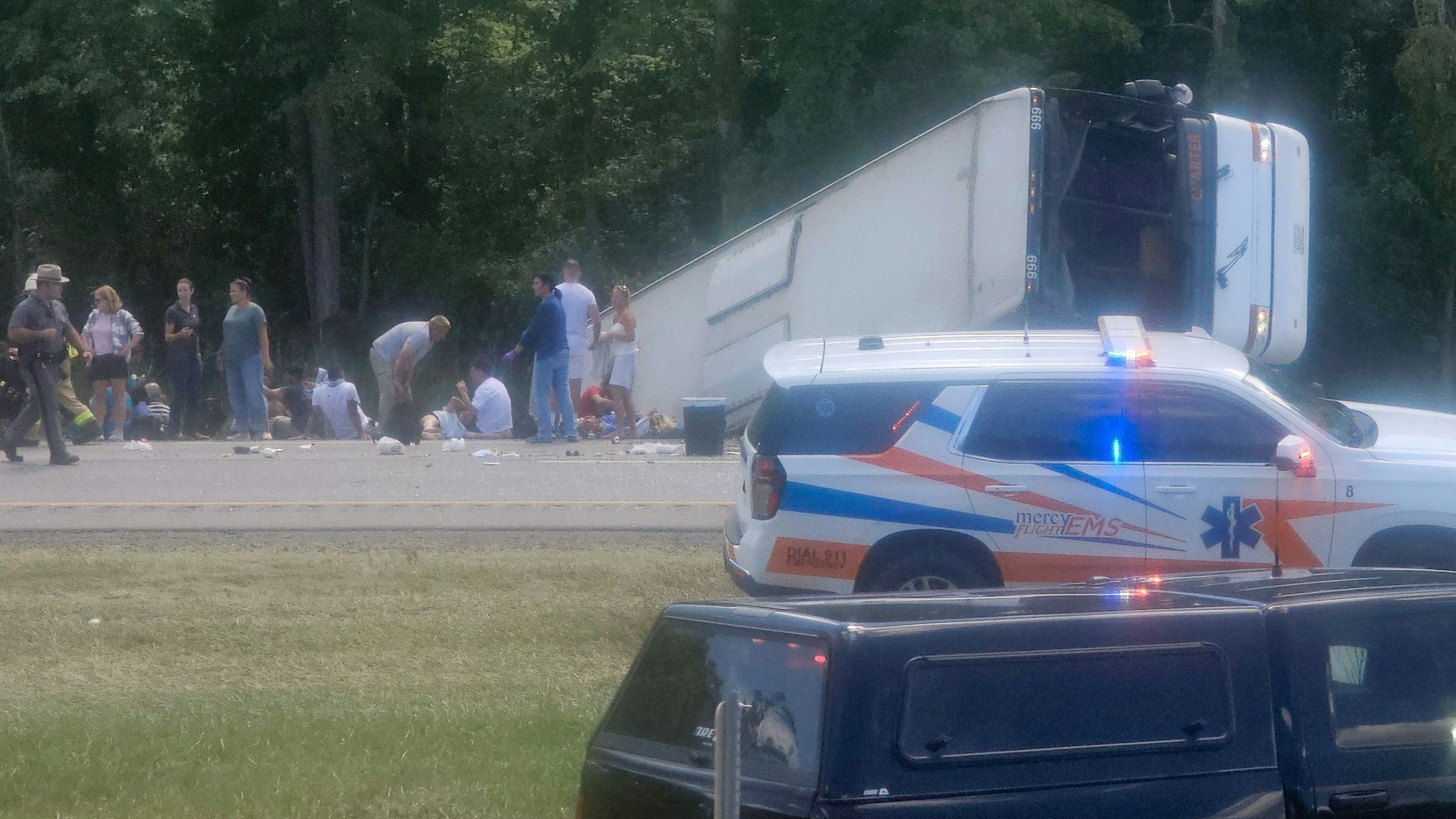 Ein Bus liegt mit der Front voraus in einem Graben, neben ihm stehen mehrere Menschen. Auch ein Polizeifahrzeug und ein Leichenwagen stehen vor Ort.