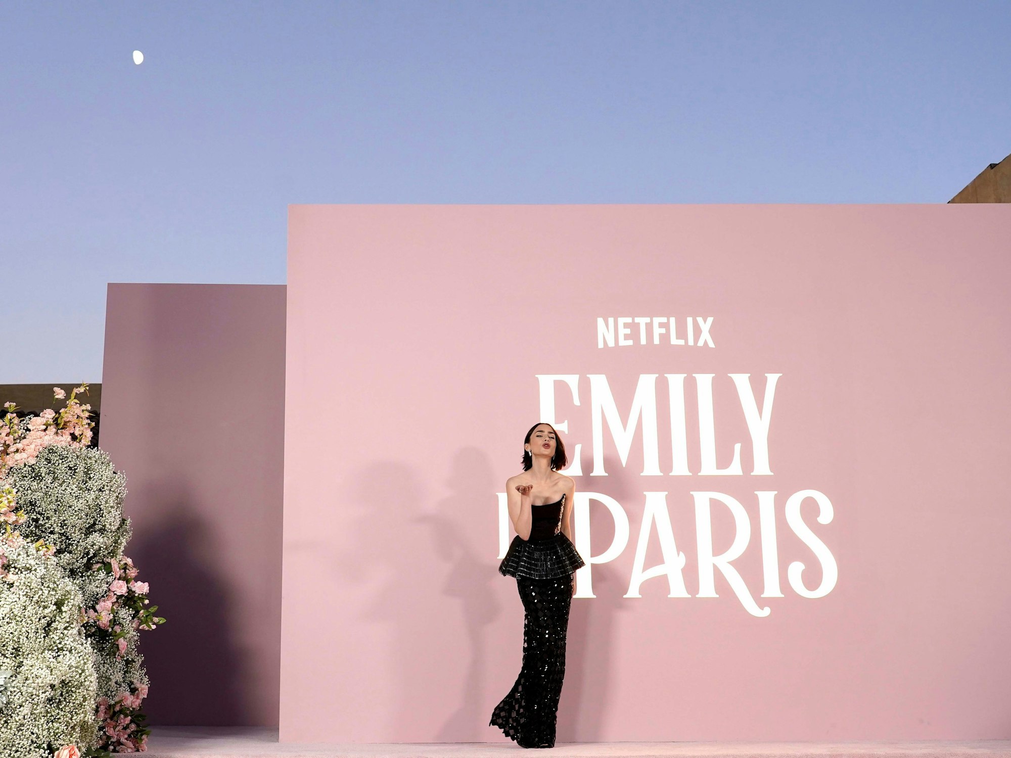 Eine Frau posiert in einem Abendkleid vor einer Wand auf der steht: Netflix Emily in Paris.