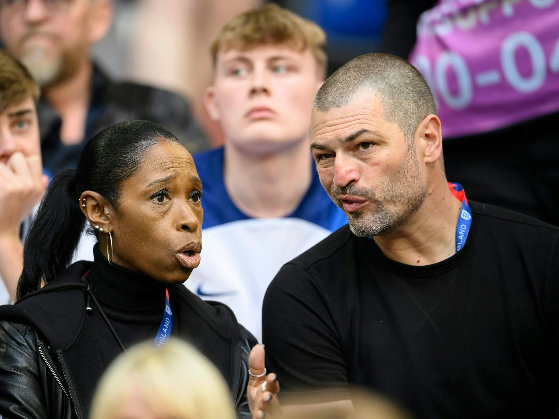 Denise Bellingham und Mark Bellingham (r.) unterhalten sich auf der Tribüne.