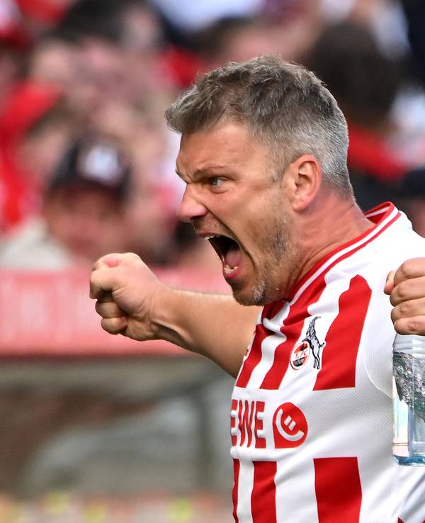 Lukas Kwasniok steht im FC-Heimtrikot an der Seitenlinie, hat eine Wasserflasche in der Hand und jubelt.