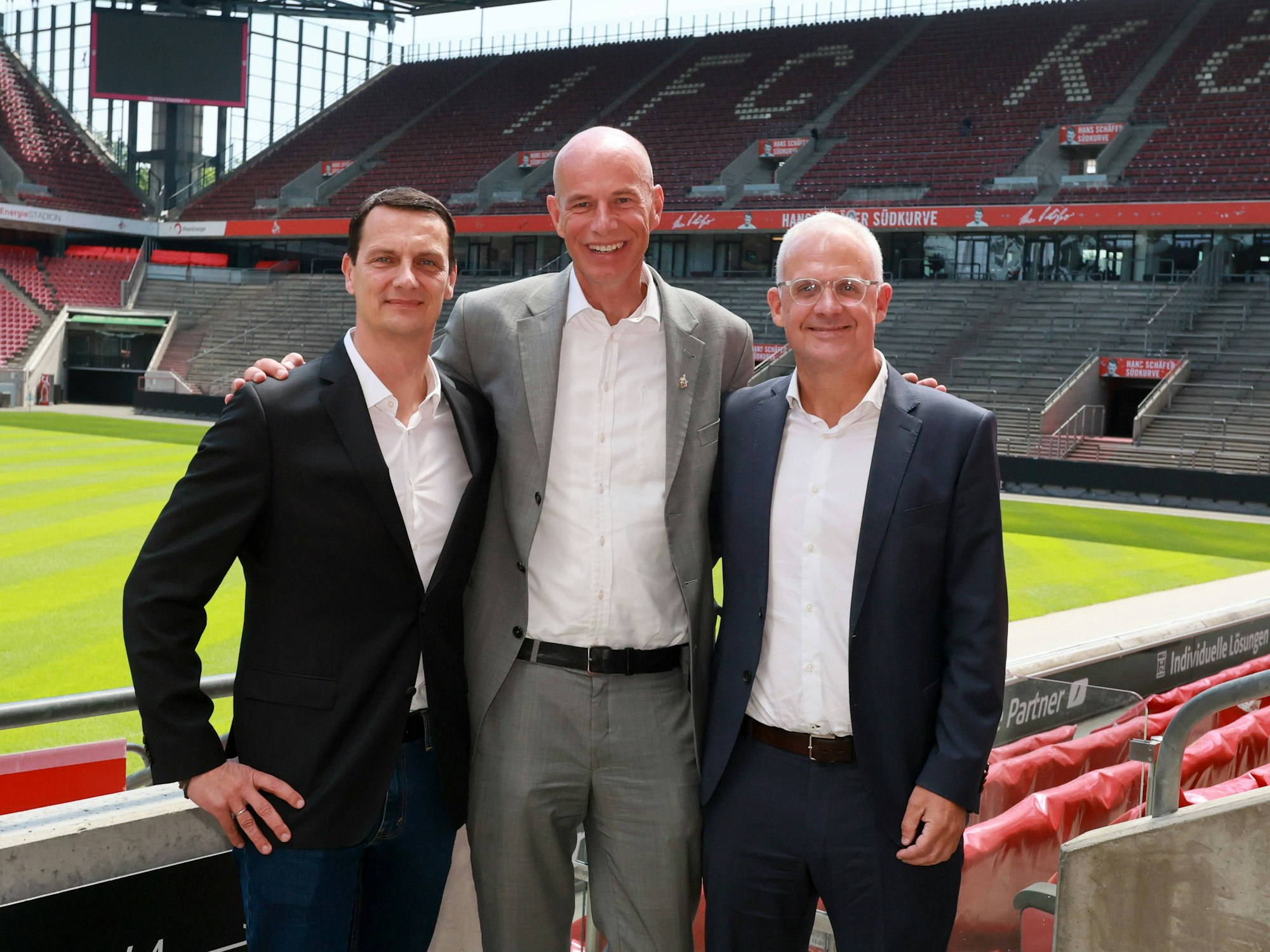 Ulf Sobeck, Jörn Stobbe und Jörg Alvermann (v.l.n.r.) stehen auf der Tribüne des Rhein-Energie-Stadions und posieren für ein Foto.