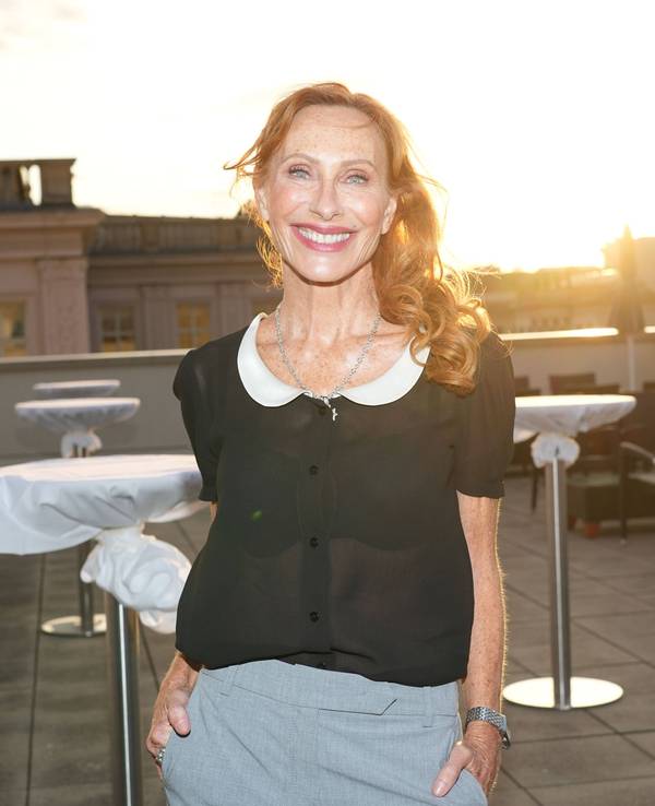 Eine rothaarige Frau lacht in die Kamera, im Hintergrund strahlt die Sonne über Hausdächern.