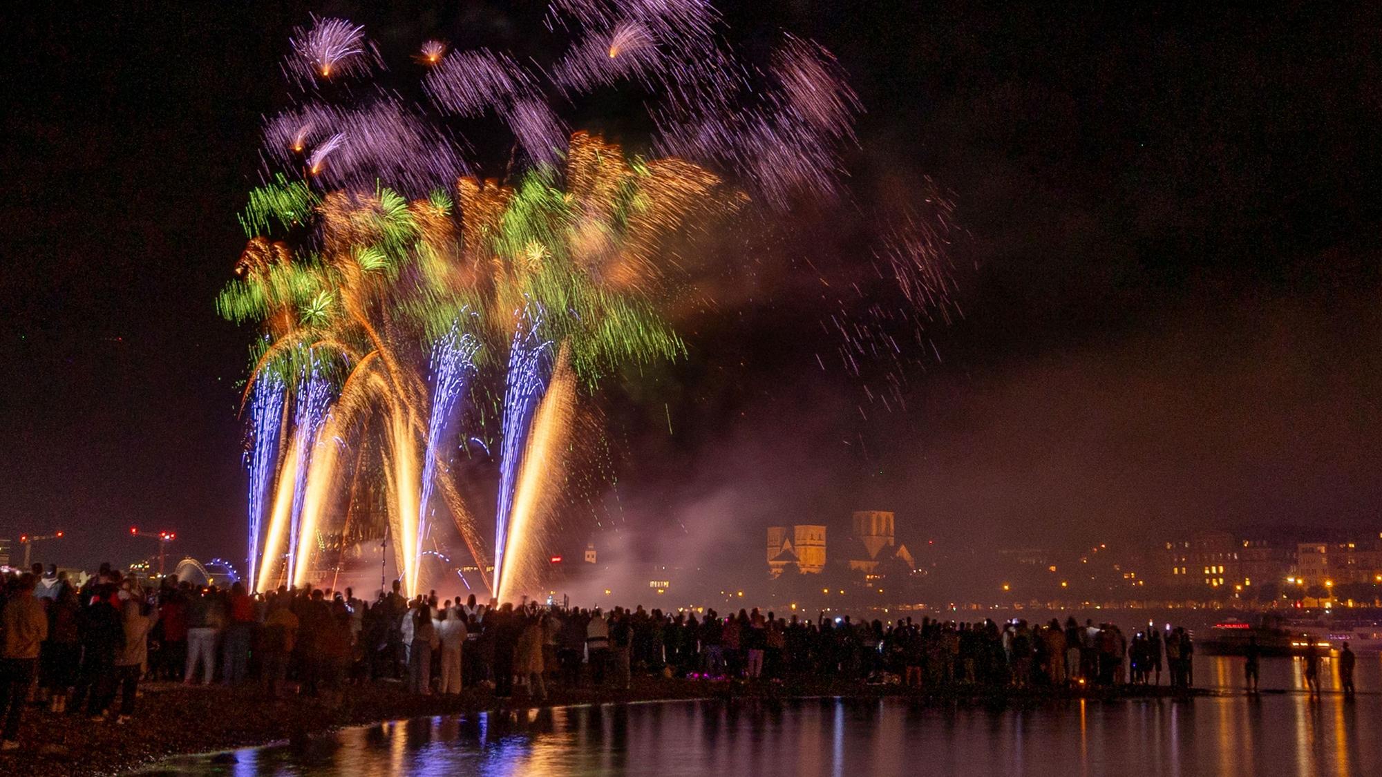 Menschen besuchen im Kölner Rheinpark das größte musiksynchrone Feuerwerk Europas.