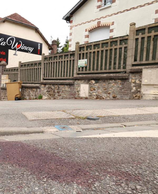 Auf einer Straße ist ein großer Blutfleck, im Hintergrund das Gebäude mit einer Werbung für eine Bar.