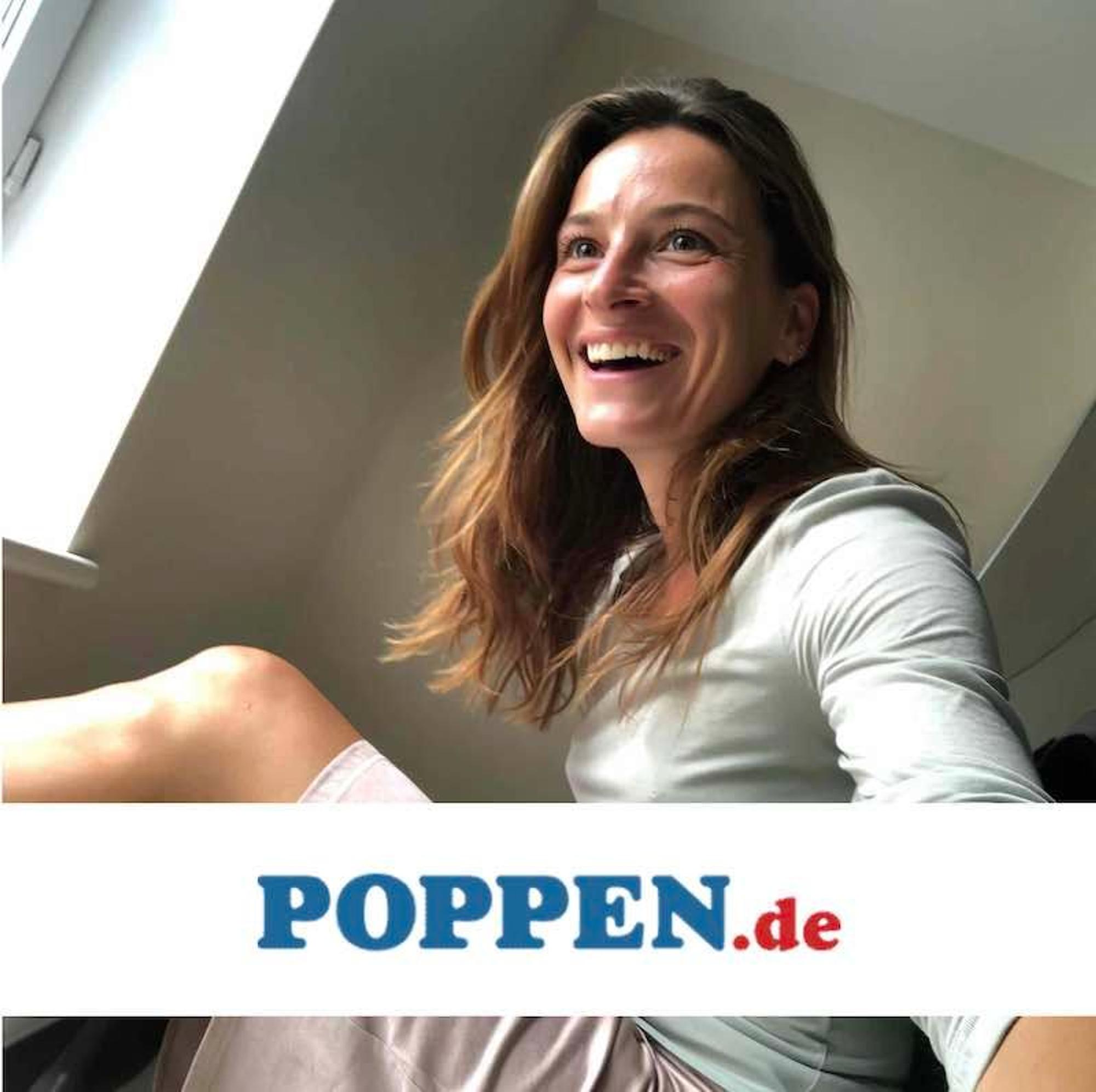 Eine hübsche Frau sitzt in einem Zimmer und lacht, während sie ein Selfie von sich macht.