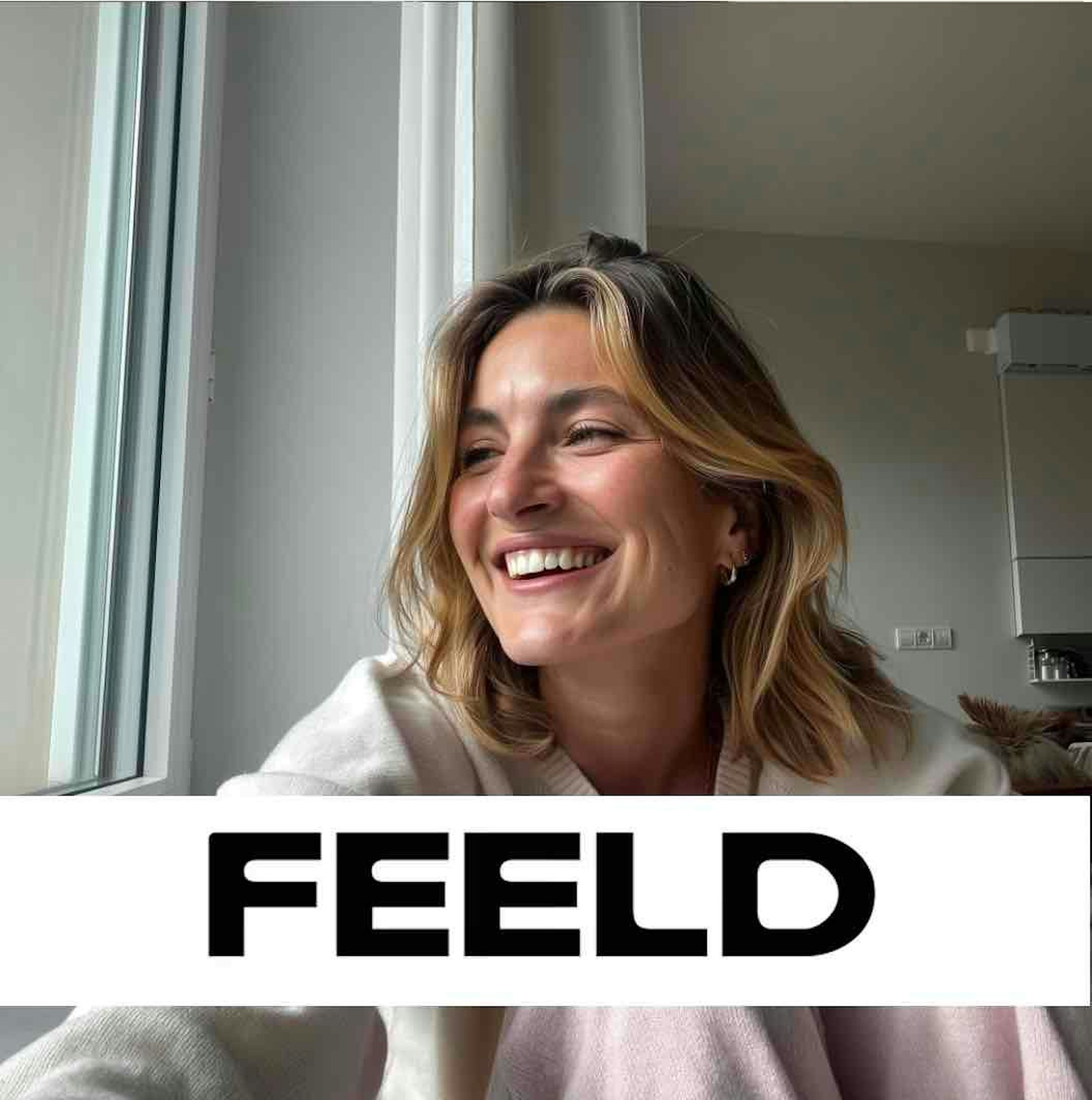 Eine lachende junge Frau blickt aus einem Fenster.