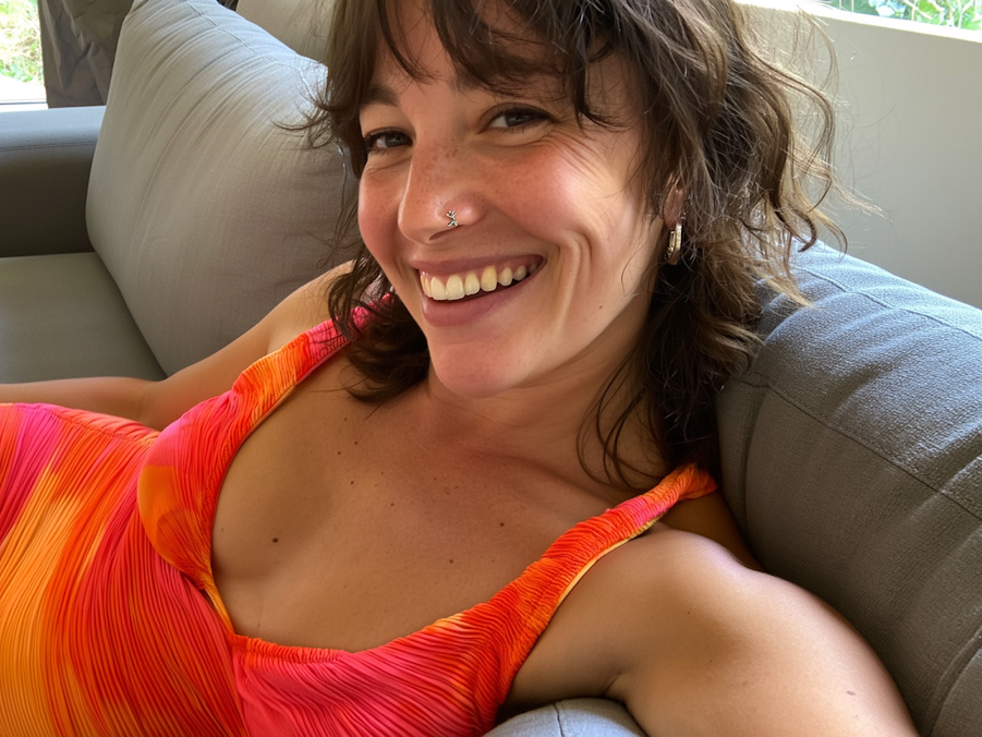 Lächelnde Frau sitzt auf einer Couch und schießt ein Selfie von sich.