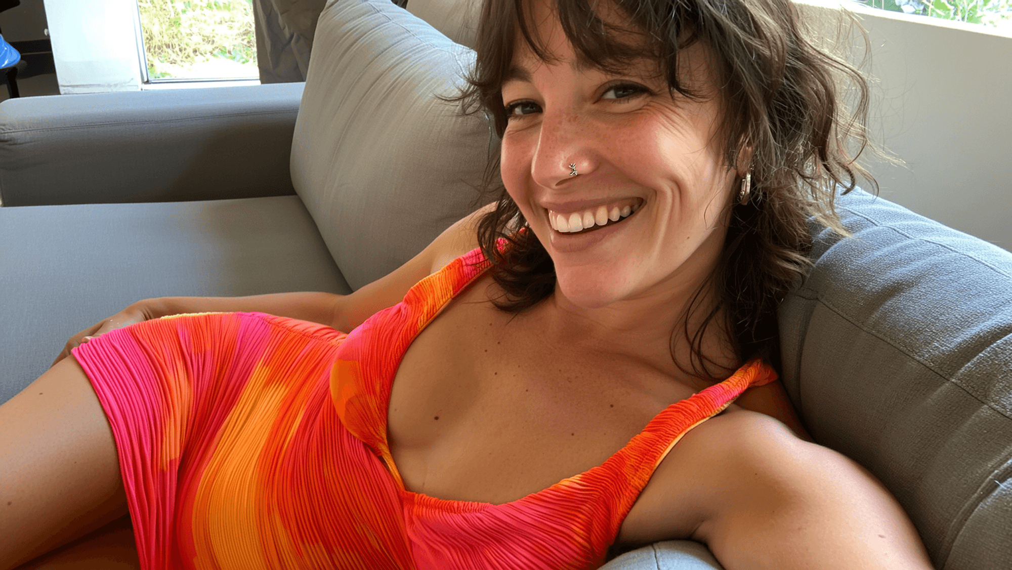 Lächelnde Frau sitzt auf einer Couch und schießt ein Selfie von sich.