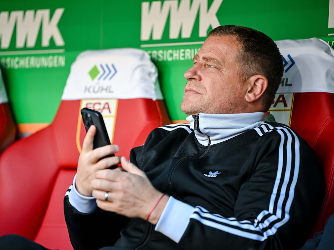 Max Eberl sitzt auf der Auswechselbank und hat sein Handy in der Hand.