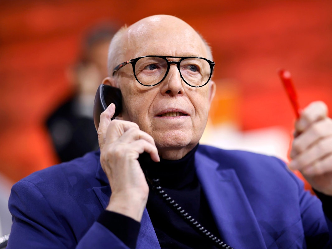 Reiner Calmund hält mit der rechten Hand ein schwarzes Telefon an sein Ohr. In der linken Hand hält er einen roten Kugelschreiber.