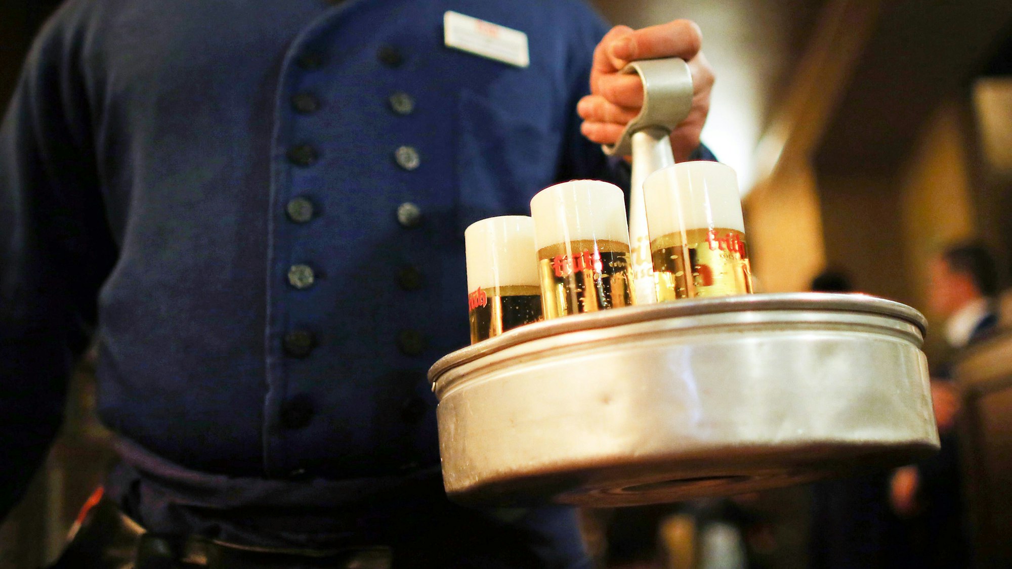 Ein Köbes mit einem Kranz Kölsch in einem Brauhaus.