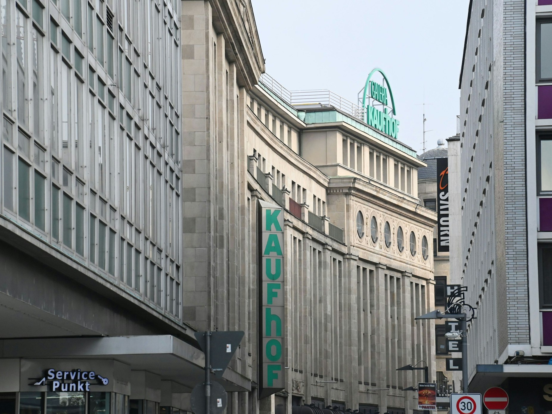 Auch einem Gebäudedach steht der Schriftzug „Galeria Kaufhof“, an der Gebäudeseite hängt der Schriftzug „Kaufhof“.