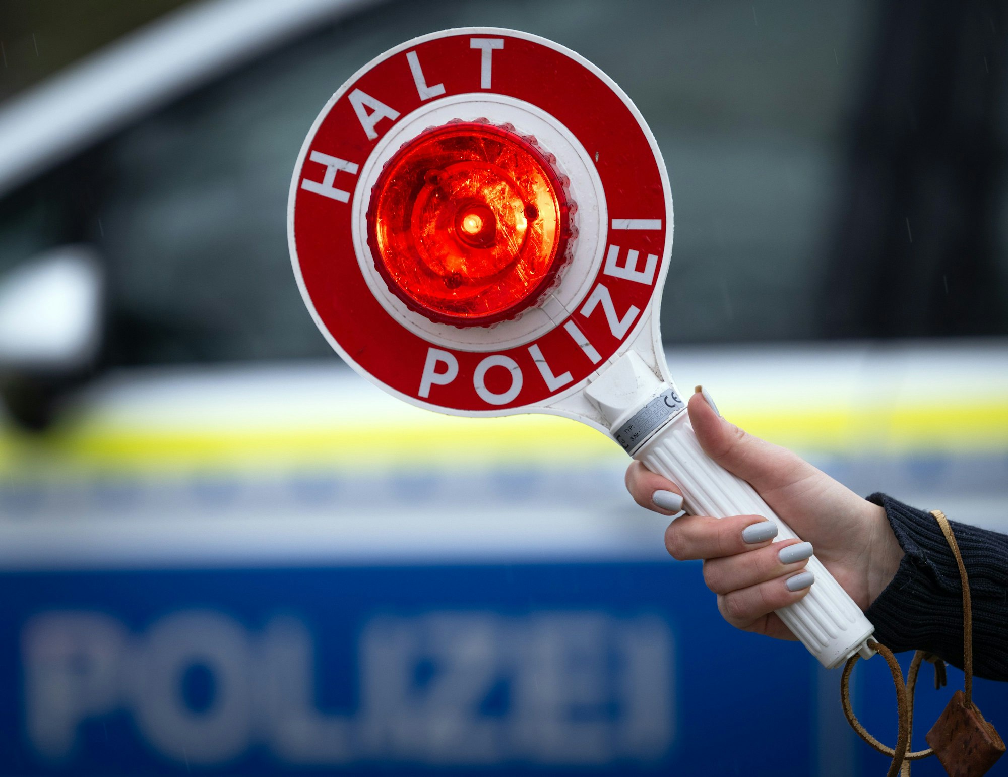 Eine Polizistin hält während einer Verkehrskontrolle eine Polizeikelle mit der Aufschrift „Halt Polizei“.