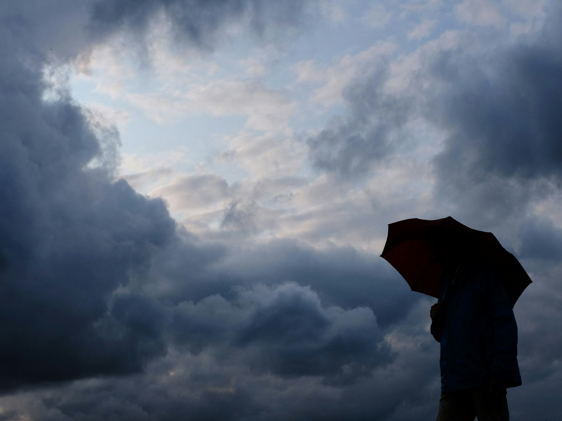 Ein Mann geht mit einem Regenschirm vor aufziehenden dunklen Wolken spazieren. (Symbolbild)