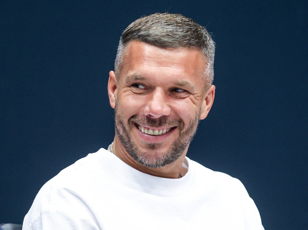 Lukas Podolski lacht bei einer Pressekonferenz.