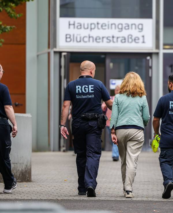 Mehrere Mitarbeiter der Schule und eines Sicherheitsunternehmens gehen auf dem Gelände der Schule, in der ein Angriff auf eine Lehrerin stattgefunden hat.