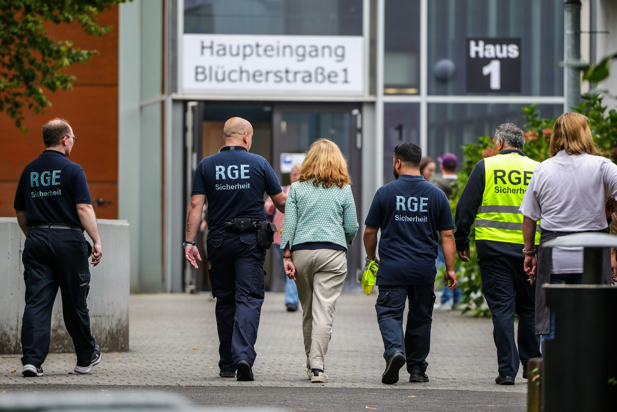 Mehrere Mitarbeiter der Schule und eines Sicherheitsunternehmens gehen auf dem Gelände der Schule, in der ein Angriff auf eine Lehrerin stattgefunden hat.