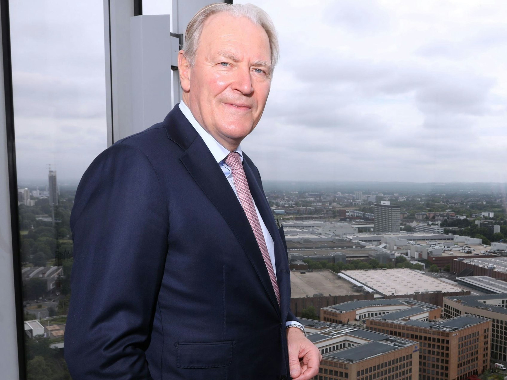 Gerald Böse, Vorsitzender der Geschäftsführung der Kölnmesse, steht an einem Fenster hoch über den Messehallen.