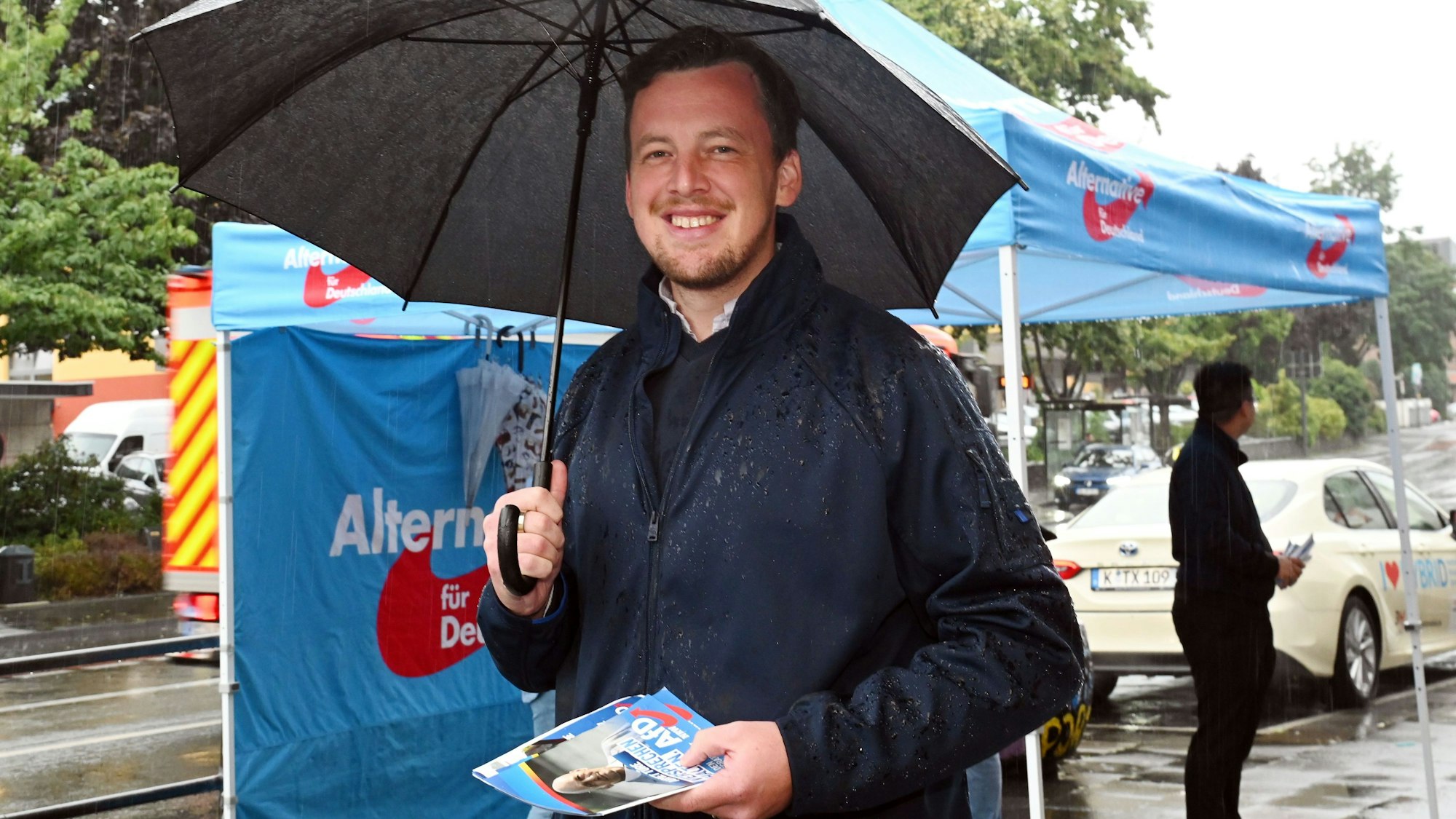 Ein Mann steht vor einem Wahlkampfstand der AfD und hält AfD-Flugblätter in der Hand.