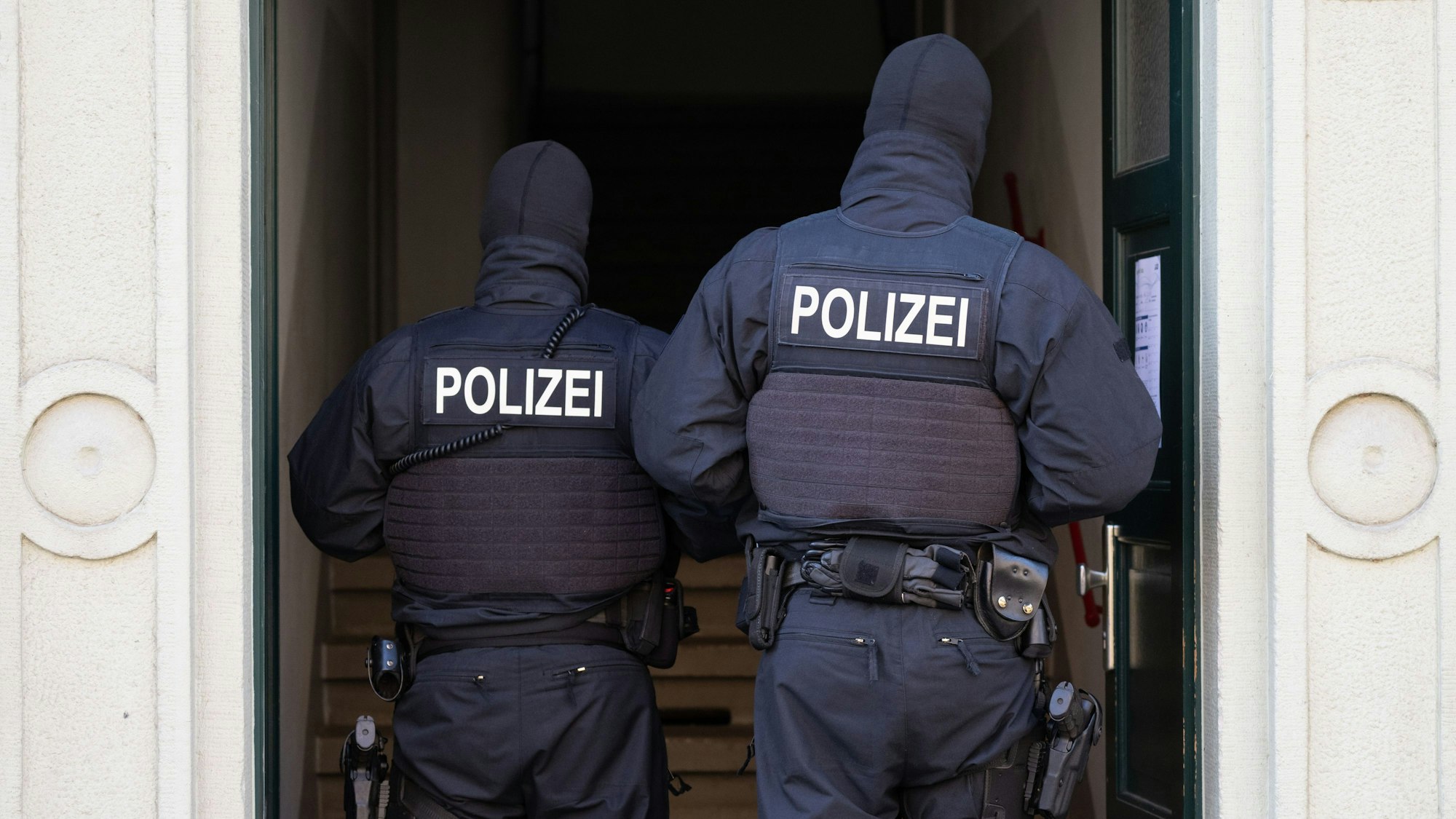 Zwei Polizisten stehen während einer Razzia in einem Hauseingang.