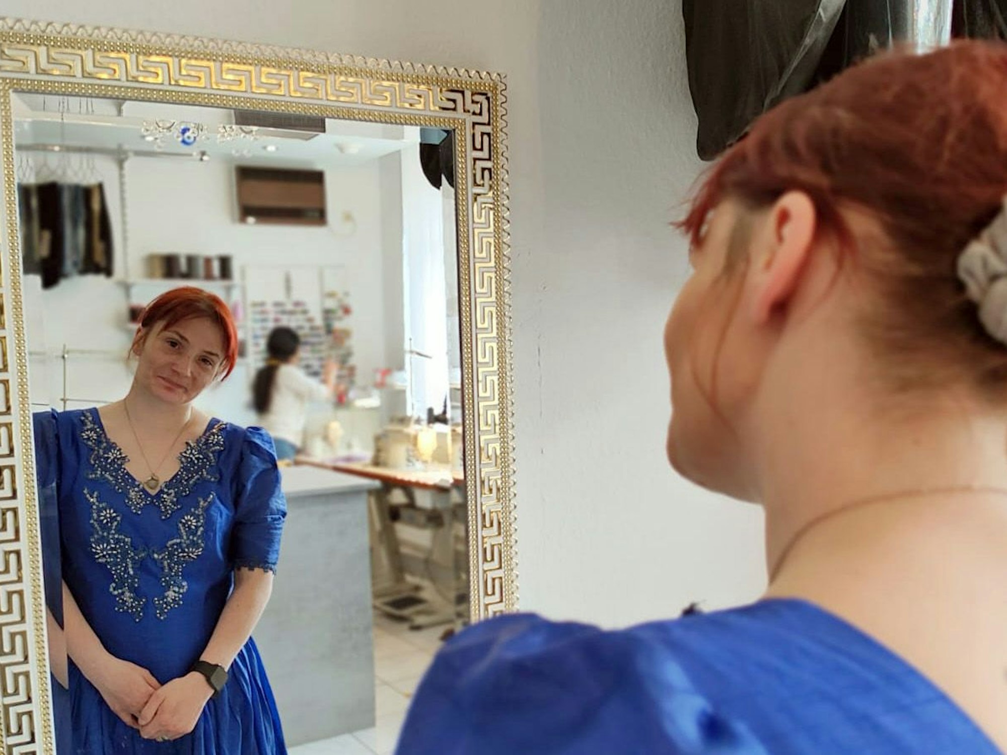 Eine Frau trägt ein Kleid und beguckt sich in einem Spiegel.