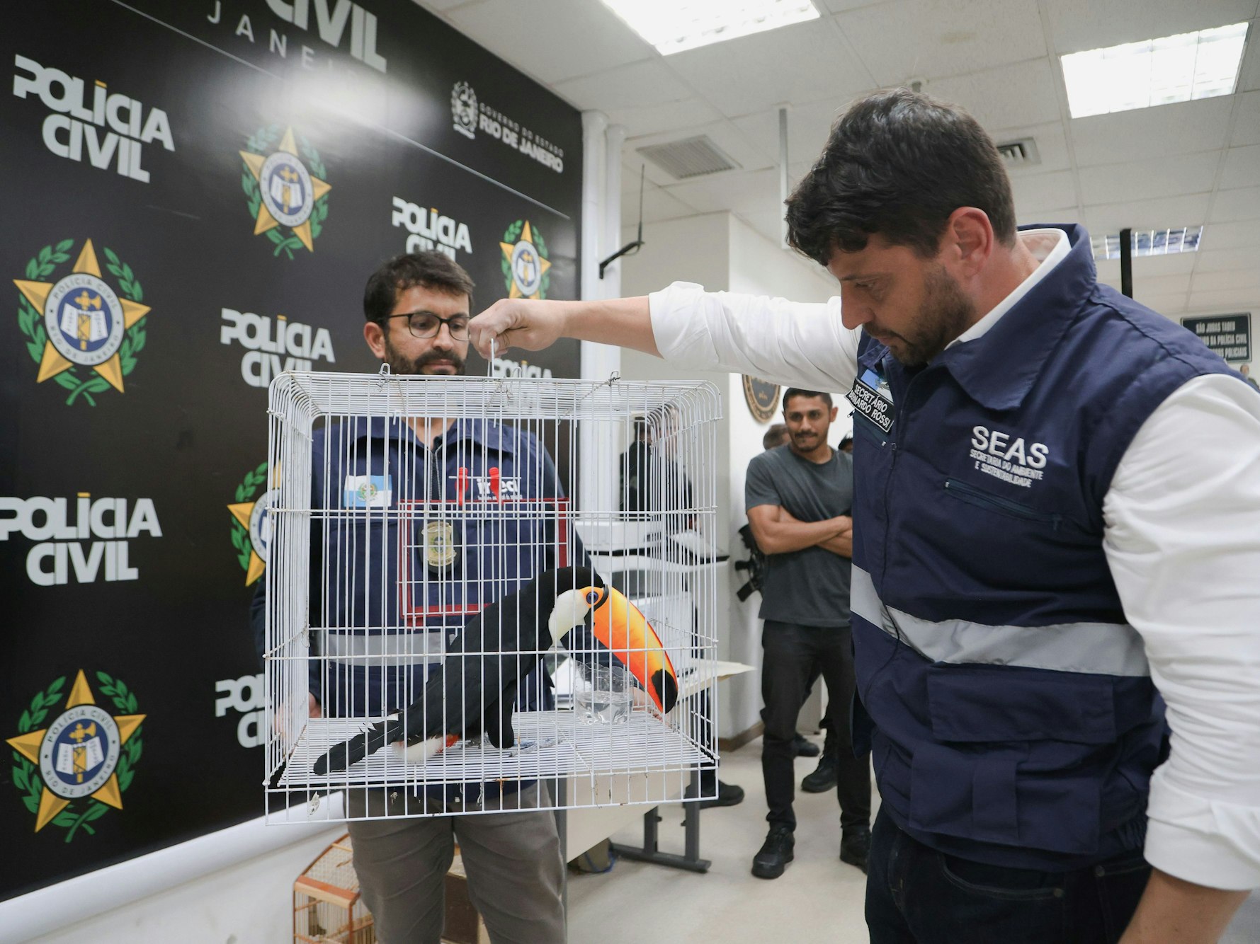 Ein Polizist hält einen Käfig mit einem exotischen Tukan in der Hand.