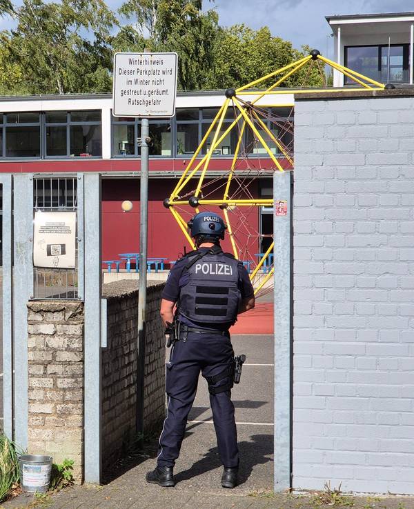 Ein Polizist steht vor einer Schule.