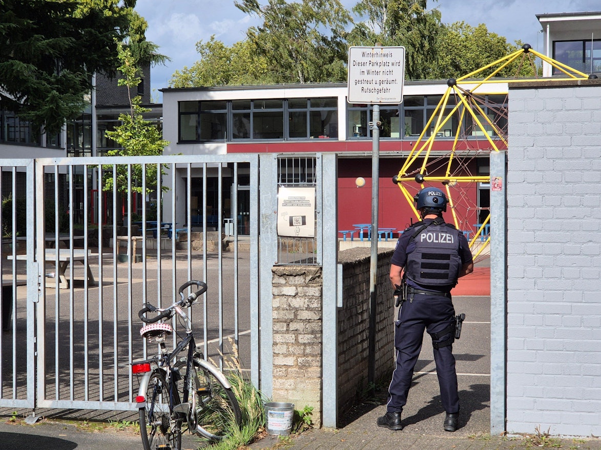 Ein Polizist steht vor einer Schule.