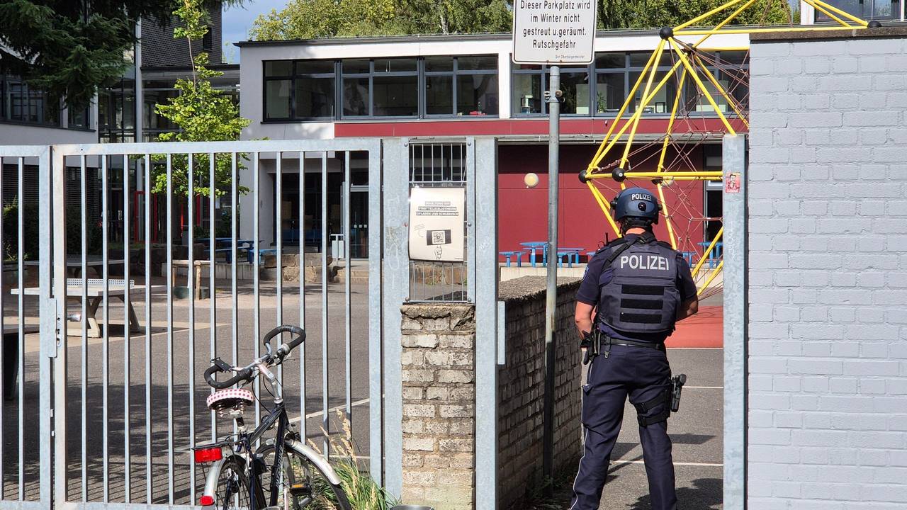 Ein Polizist steht vor einer Schule.
