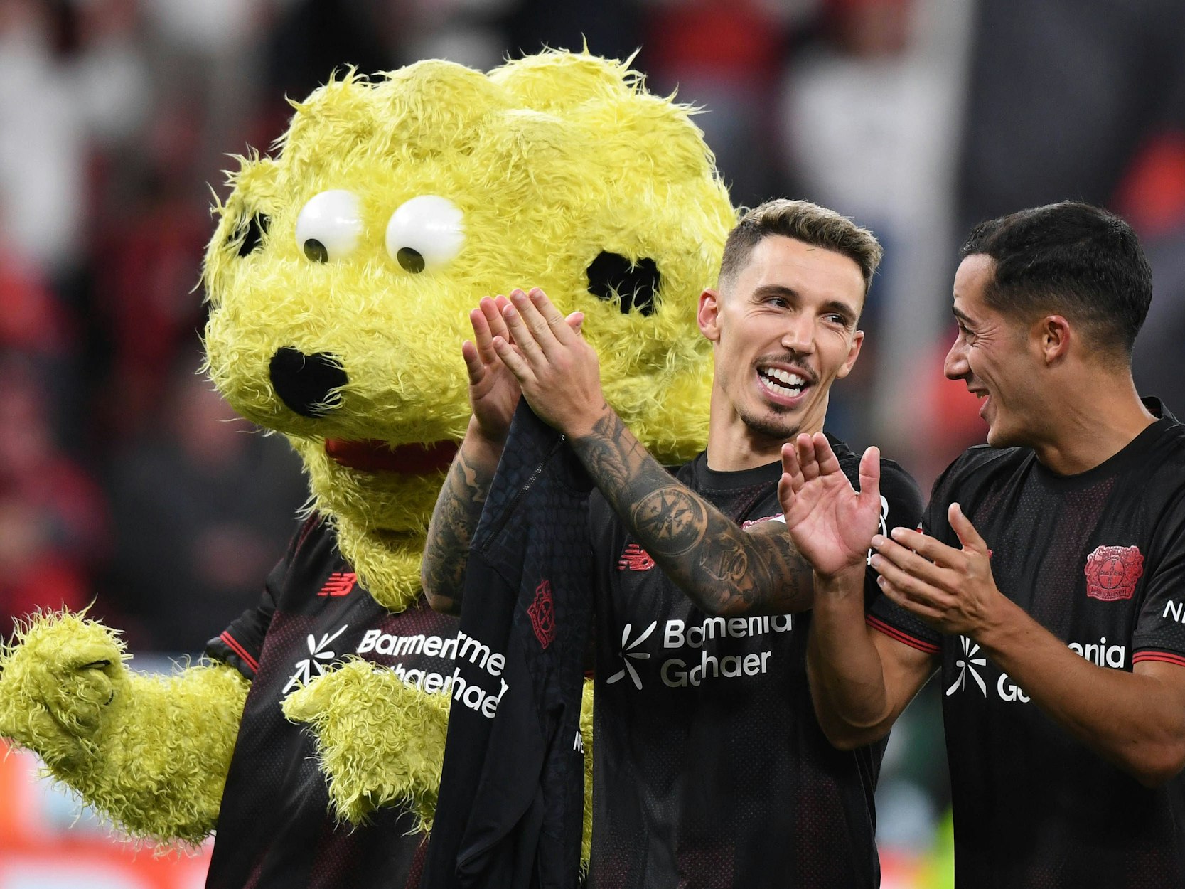 Lucas Vázquez (r.) und Alejandro Grimaldo applaudieren den Fans. Daneben steht Leverkusen-Maskottchen Brian the Lion.