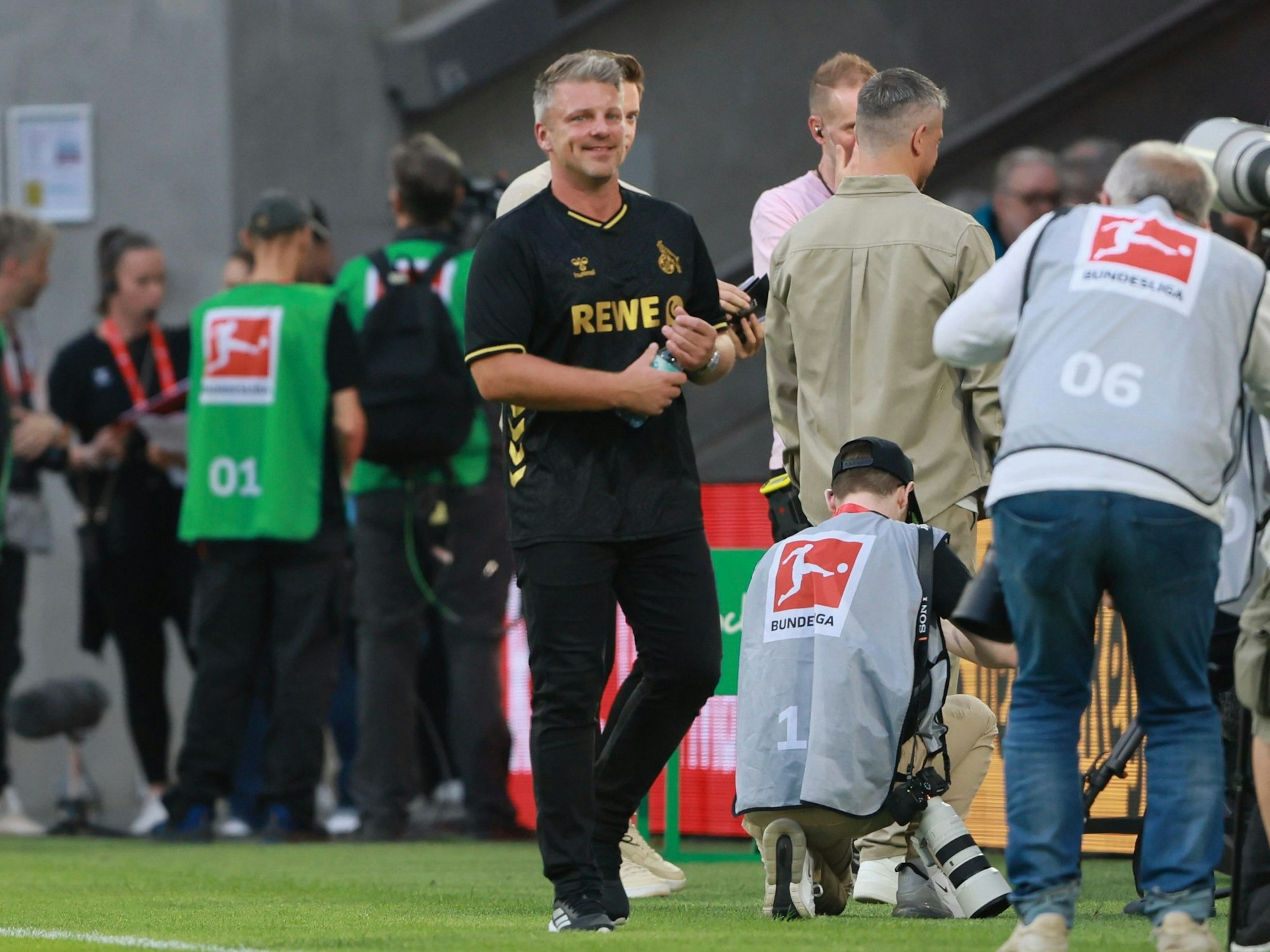 Lukas Kwasniok steht an der Seitenlinie und dreht eine Wasserflasche mit seinen Händen auf.