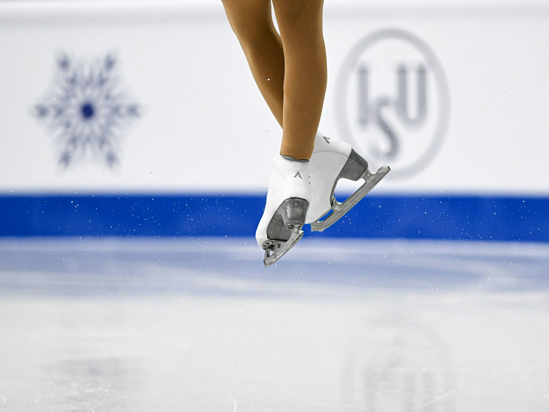 Die Füße einer Eiskunstläuferin beim Sprung in Schlittschuhen.