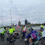Radfahrerinnen und Radfahrer radeln über den Rhein, vorweg ein Polizeifahrzeug.