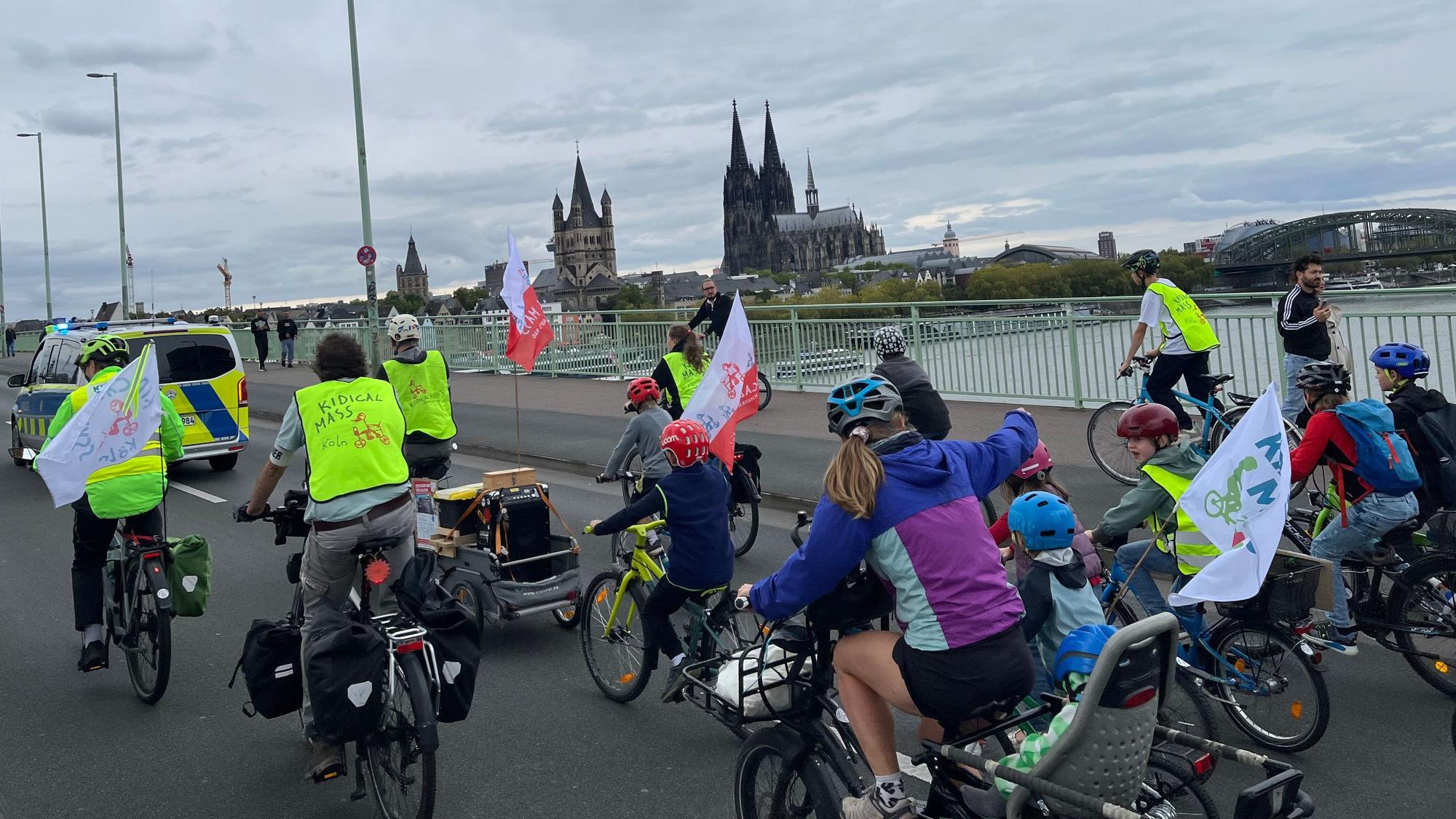 Radfahrerinnen und Radfahrer radeln über den Rhein, vorweg ein Polizeifahrzeug.