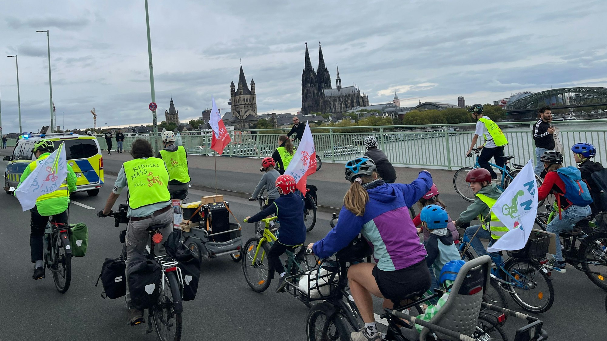 Radfahrerinnen und Radfahrer radeln über den Rhein, vorweg ein Polizeifahrzeug.