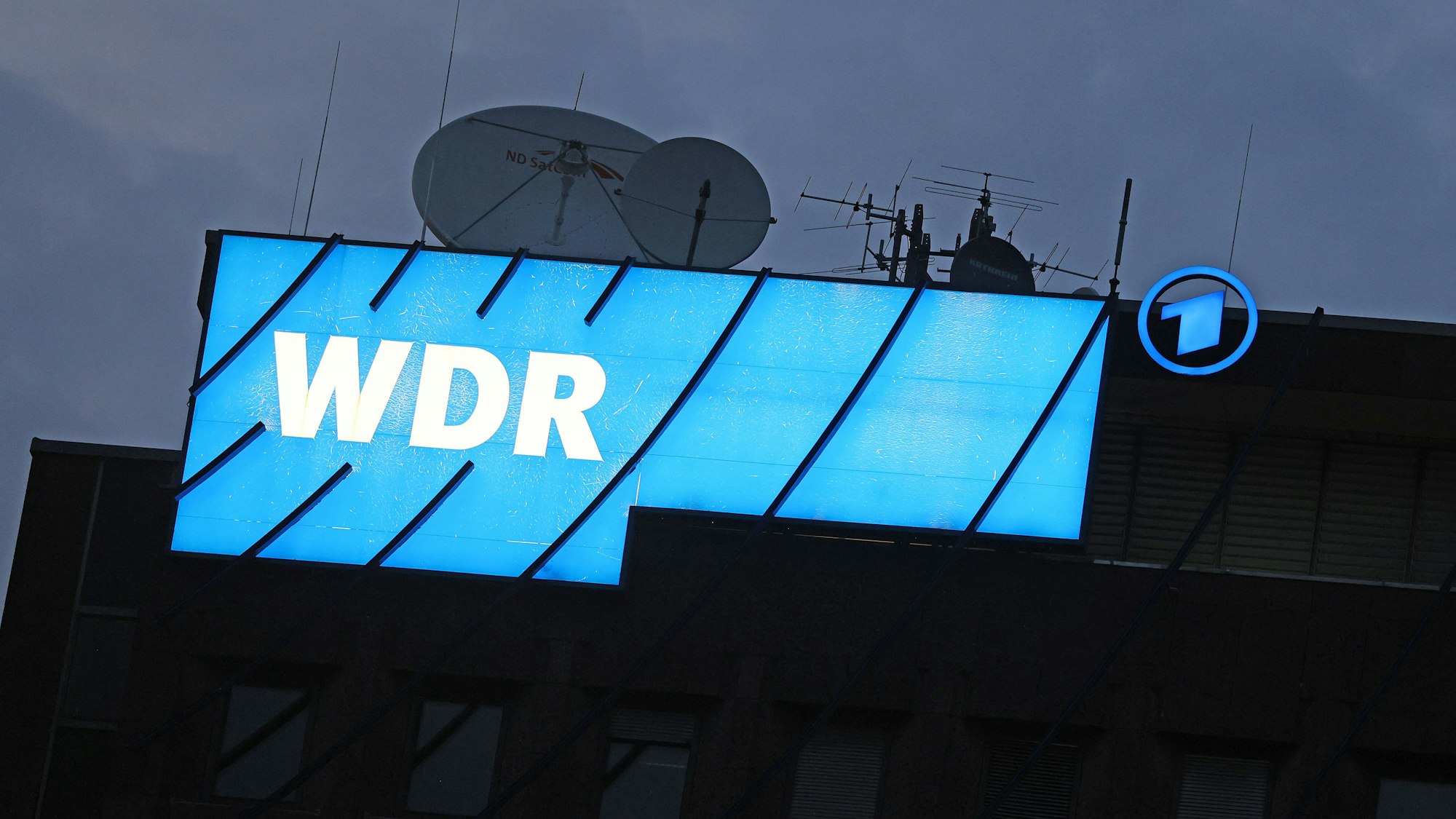 Ein Logo des WDR leuchtet auf dem Dach des Senders in Köln.