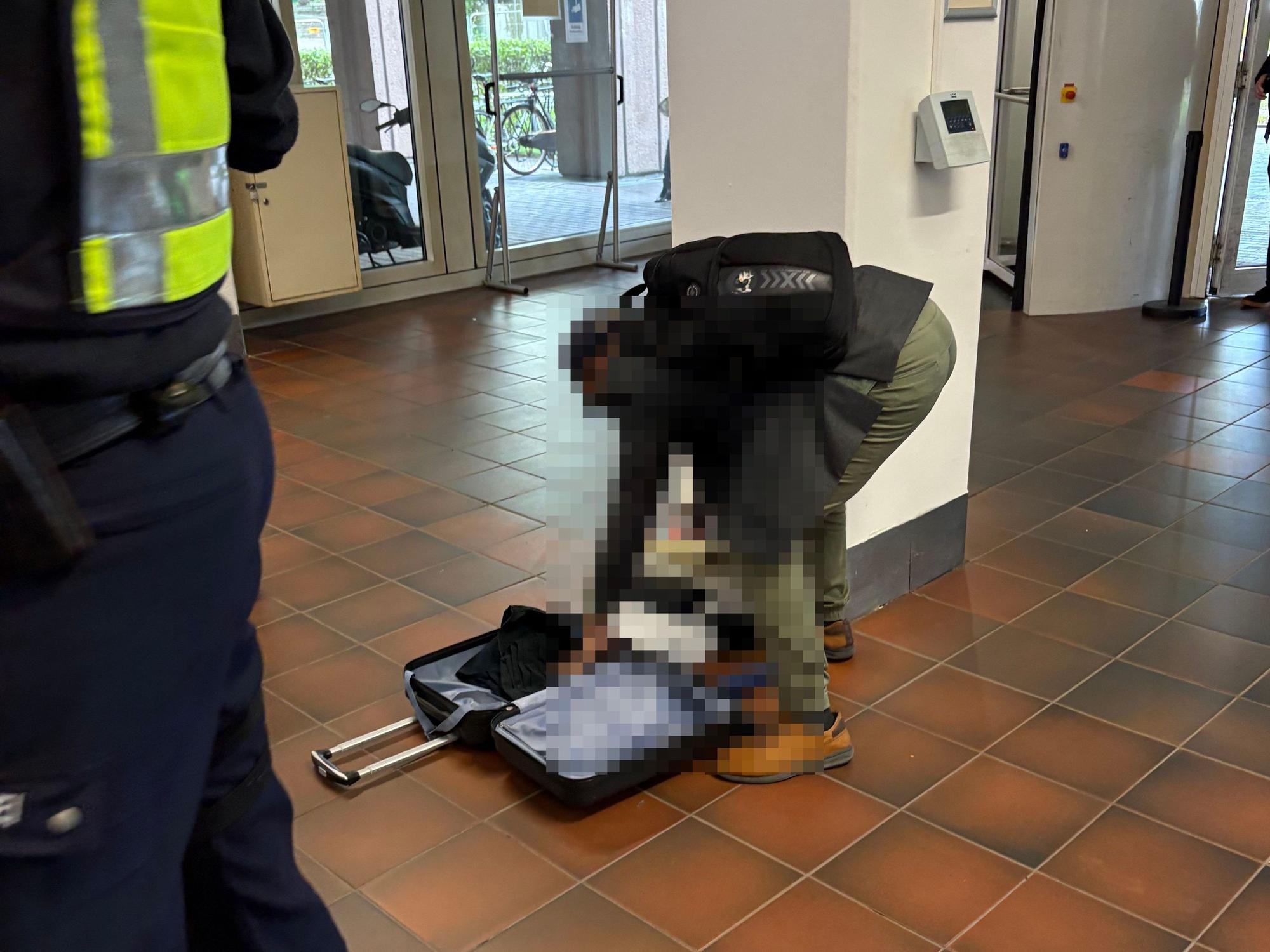 Ein Mann hat im Gerichtsfoyer einen Koffer geöffnet und wühlt in Kleidungsstücken.