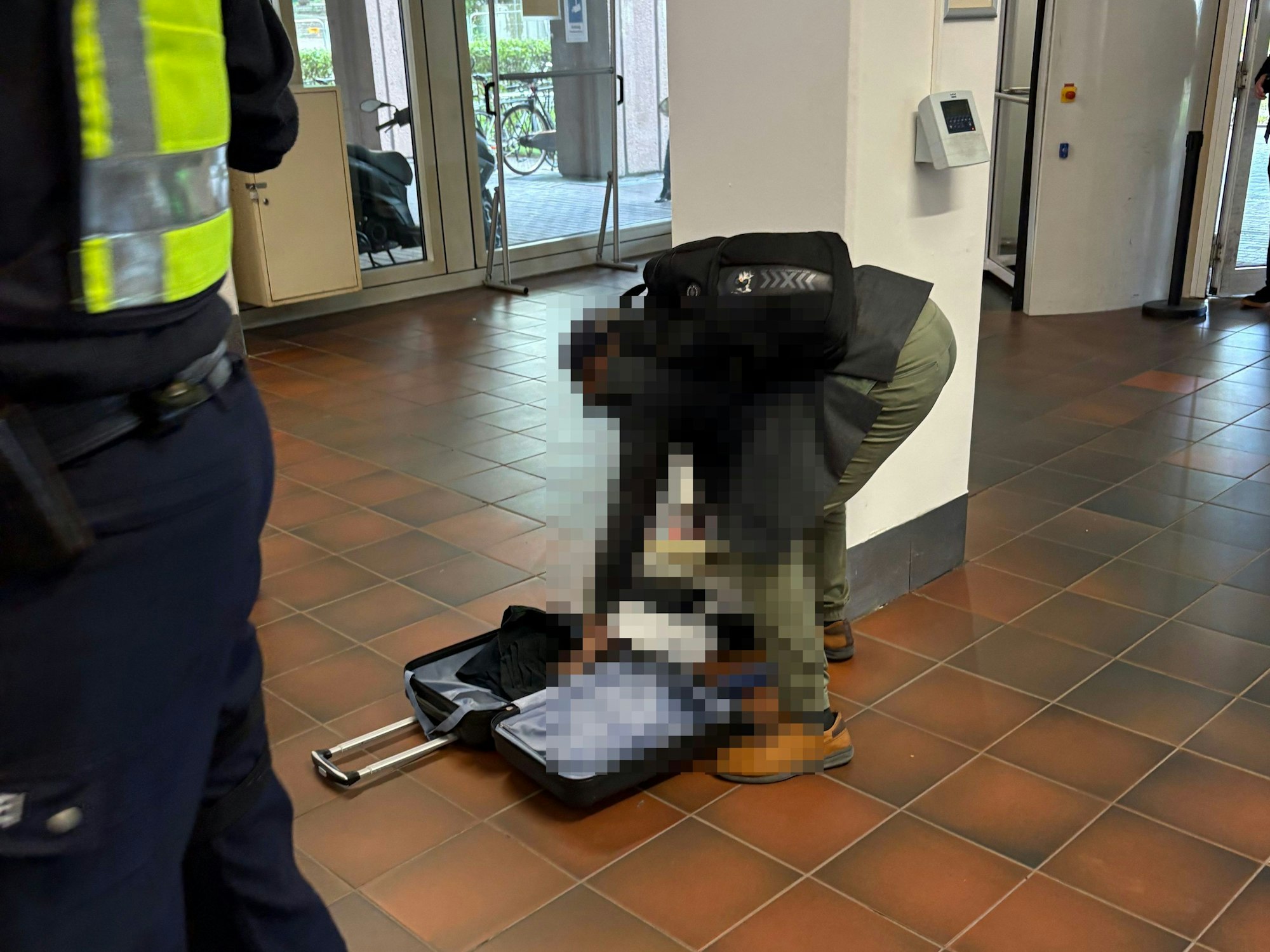 Ein Mann hat im Gerichtsfoyer einen Koffer geöffnet und wühlt in Kleidungsstücken.