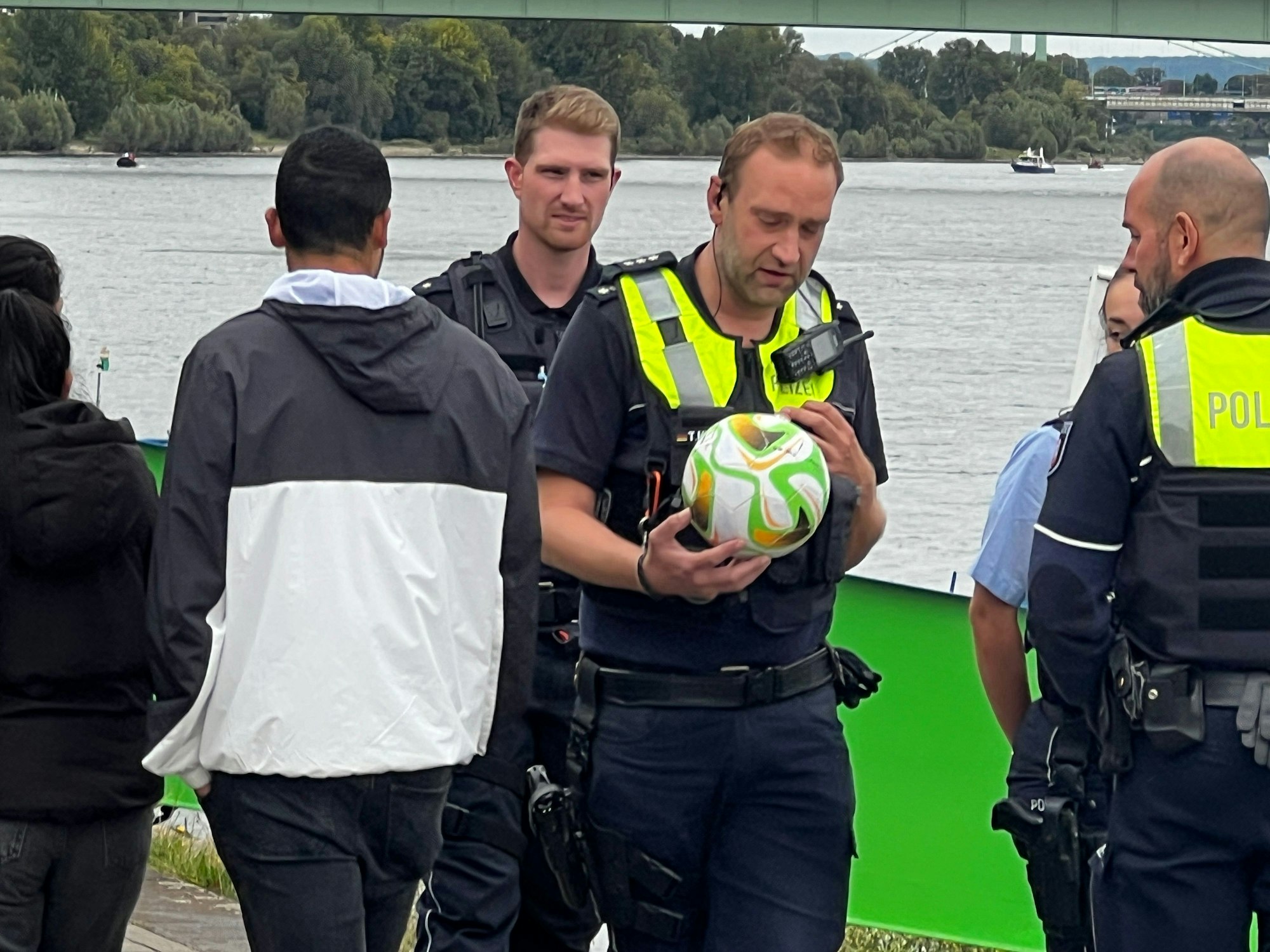 Einsatzkräfte der Polizei stehen am Rhein, ein Polizist hält einen Ball in der Hand.